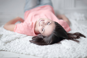 close up. young woman lying on white carpet in living room and looking at camera