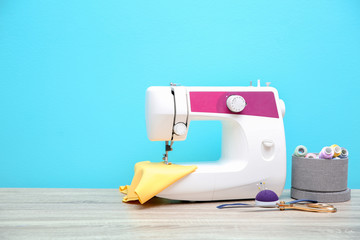 Sewing machine on table against color background