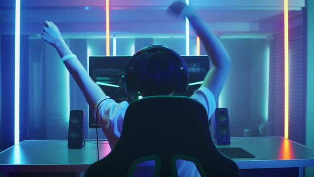 Professional Gamer Playing and Winning in First-Person Shooter Online Video Game on His Personal Computer. He's Talking with His Team Through Headset. Room Lit by Neon Lights in Retro Arcade Style. 