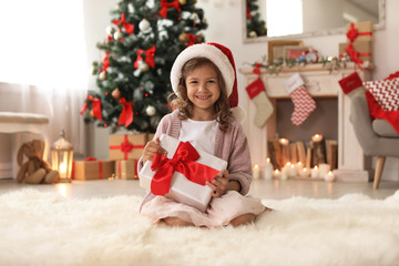Fototapeta na wymiar Cute little child in Santa hat with Christmas gift box at home