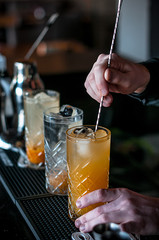 bartender barmen with cocktail preparing orange cocktail at bar. alcohol drinks, job people and luxury night club concept