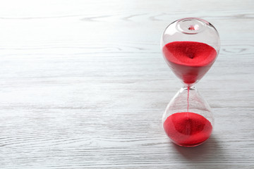 Hourglass with flowing red sand on wooden background. Time management