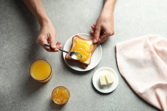 Woman spreading jam on toast bread at table, top view