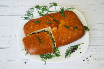A pie with meat and one piece of it lie on a white plate