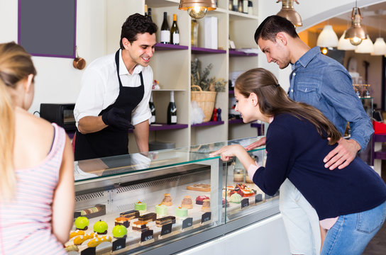 Couple with woman friend are choosing delicious cakes from showcase