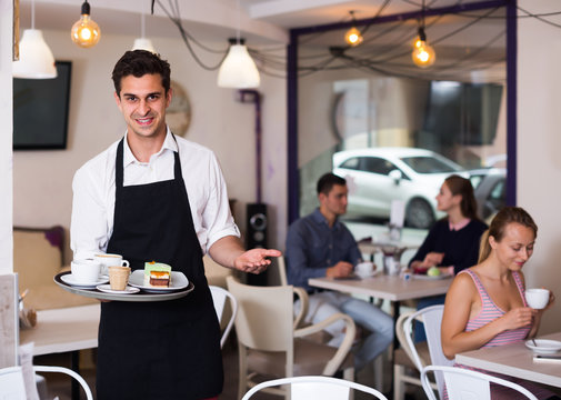 Portrait of young waiter inviting to coffee
