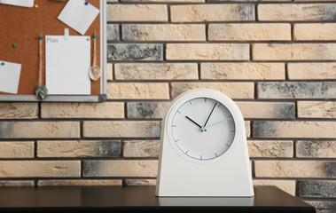 Stylish clock on table near brick wall. Time management
