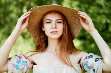 A sophisticated red-haired girl in a simple linen dress, in a light wide-brimmed hat. Model look. Natural beauty. Artistic portrait