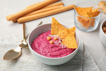 Ceramic bowl with tasty beet hummus and chips on light table