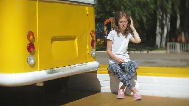 young woman outdoors by yellow vagon car listening music in headphones using smartphone - relaxing, enjoying, concept of technology and travel