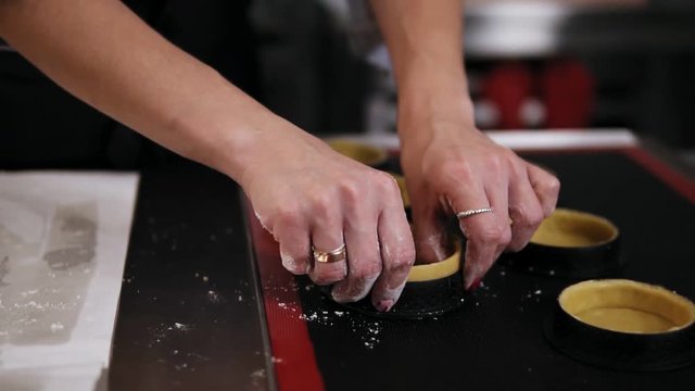 Female hands of professional confectioner forming dough for baking tartlets. Black working surface. Indoors, culinary master class