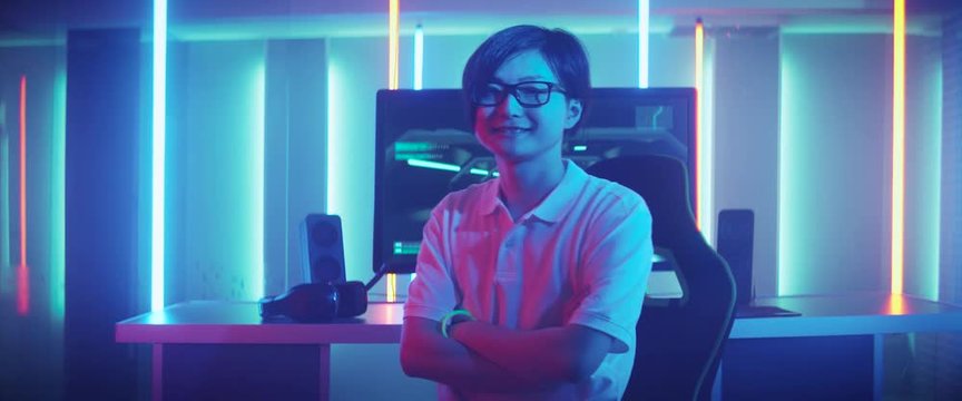 East Asian Pro Gamer Playing in Video Games Turns around and Smiles After winning Online Tournament. Stylish Neon Retro Arcade Room. Shot with Anamorphic Lens.