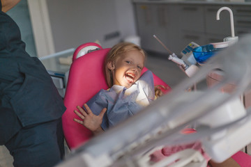partial view of dentist and kid sticking tongue out in chair at dentist office