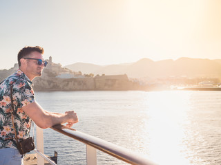 Attractive guy with a vintage camera on the deck of a cruise liner against a background of blue, sea waves, sunset and shoreline. Concept of sea cruises and rest