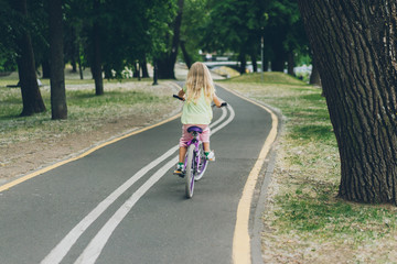 back view of blond child riding bicycle on road in park