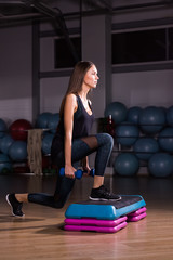 Young woman performs step cardio with dumbbells in a gym