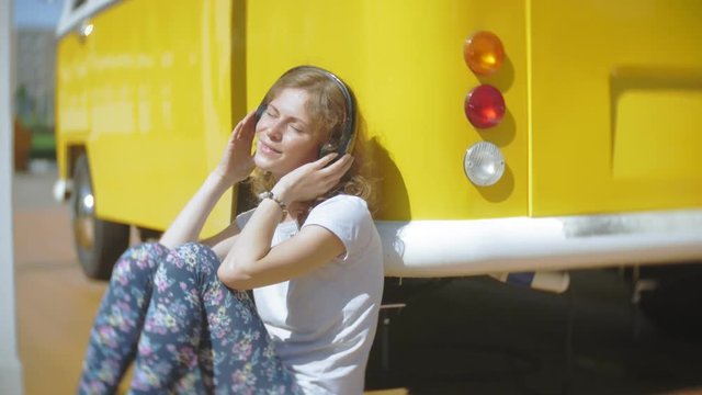 young woman outdoors by yellow vagon car listening music in headphones using smartphone - relaxing, enjoying, concept of technology and travel