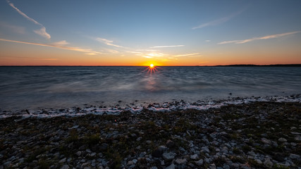 dramatic sunrise over the baltic sea with rocky beach and trees on the shore