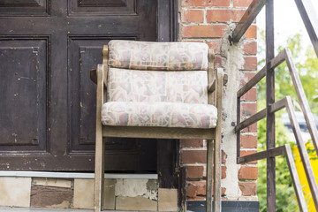 old ragged armchair in front of a wooden door with brick wall