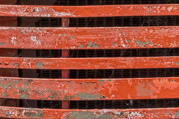 Red metal bars strech horizontially of a metal structure. The paint is pealing with rust is showing below.