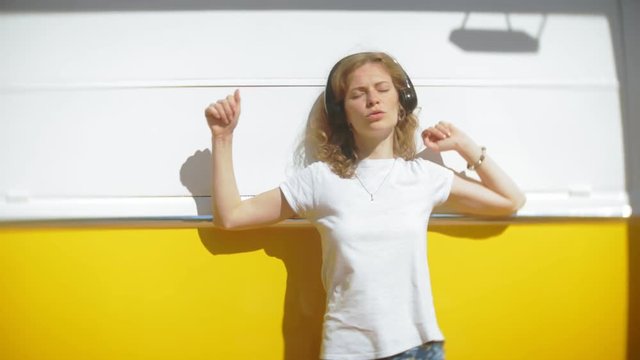 young woman outdoors by yellow vagon car listening music in headphones using smartphone - relaxing, enjoying, concept of technology and travel