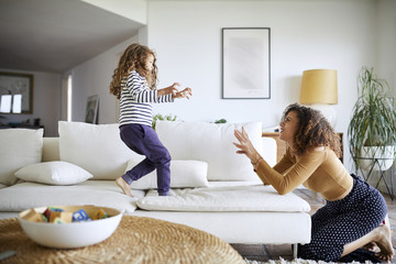 Side view of happy mother playing with daughter in living room