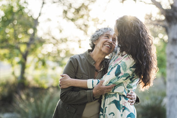 Happy mother and daughter embracing while standing at park