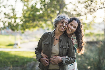 Portrait of smiling daughter embracing mother while standing outdoors