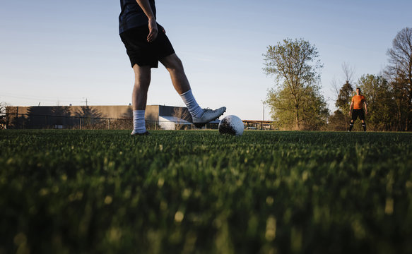 Low section of man playing soccer with male friend on grassy field against clear sky at park