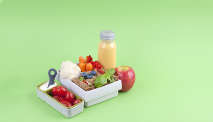Office lunch in a box and juice with fruit on a green background. Free space for text. Copy space.