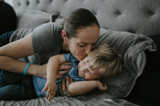 Happy mother kissing son while lying on bed at home