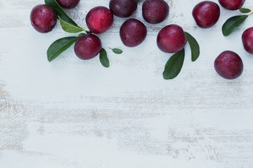 Fresh plums with leaves on white rustic wooden table background.