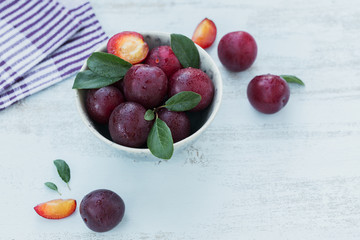 Fresh plums with leaves on rustic wooden table background.