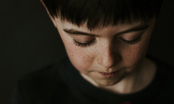High angle close-up of boy with freckles over black background