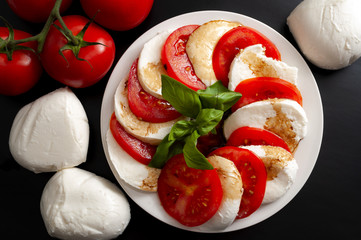 Mediterranean cuisine, fresh vegetarian food and italian culinary art concept with Caprese salad made of mozzarella cheese, rraw tomatoes and basil leafs isolated on black background