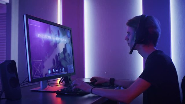 Arc Shot of the Professional Gamer Playing in First-Person Shooter Online Video Game on His Personal Computer. Room Lit by Neon Lights in Retro Arcade Style. 