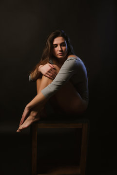 Alone sad brunette model sitting on a chair in the dark room