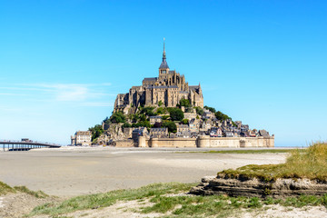 Fototapeta na wymiar General view of the Mont Saint-Michel tidal island, located in France on the limit between Normandy and Brittany, from the bay at low tide under a summer blue sky.