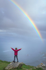 Girl on the top of a rock looking at rainbow