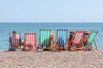 Rear View of Group of People Seated in Six Striped Deckchairs at the Seaside on a Bright Sunny...