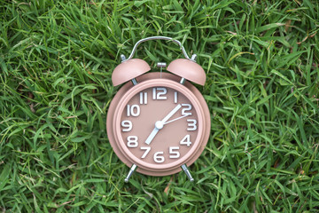 alarm clock on fresh green grass field in early morning , spring time