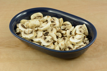 Chopped fresh white button mushrooms in dark blue oval dish