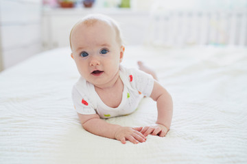 Adorable baby girl lying on bed on tummy