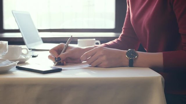 Hands of young businesswoman filling out contract form when sitting at table in cafe or restaurant