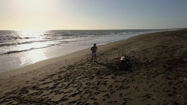Aerial footage - Jogger on a lonely sand beach runs at sunset with light reflection on the sea surface