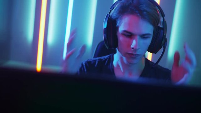 Young Pro Gamer Playing in Online Video Game, Puts on His Headset, talks with Team Players through Microphone. 