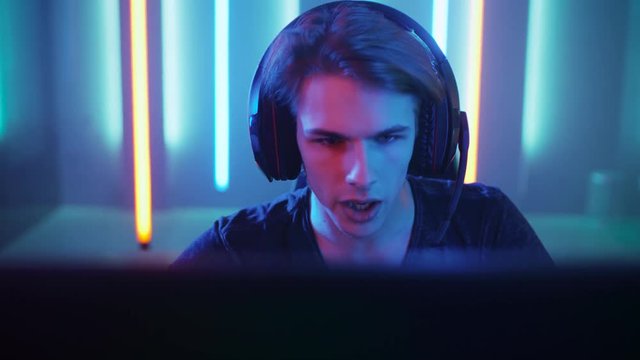 Young Pro Gamer Playing in Online Video Game, talks with Team Players through Microphone. Neon Colored Room. e-Sport Cyber Games Internet Championship.