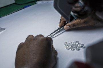 Man's hands inspecting rough diamonds with forceps.