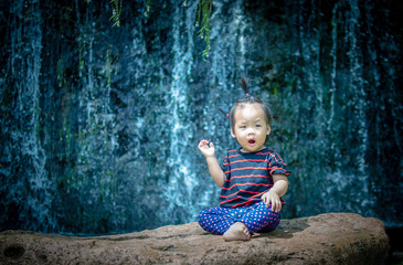 Naklejka premium child girl raise her hand sitting on the rock