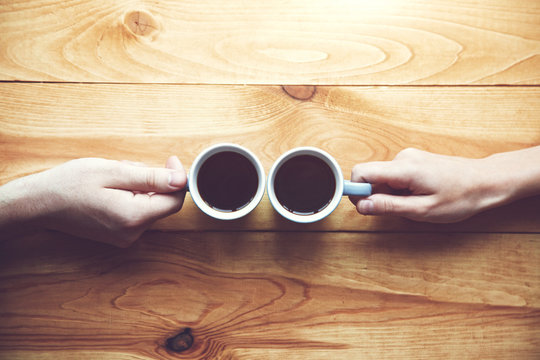 Hands Of Couple With Two Cups Of Morning Coffee On Wooden Table. View From Above